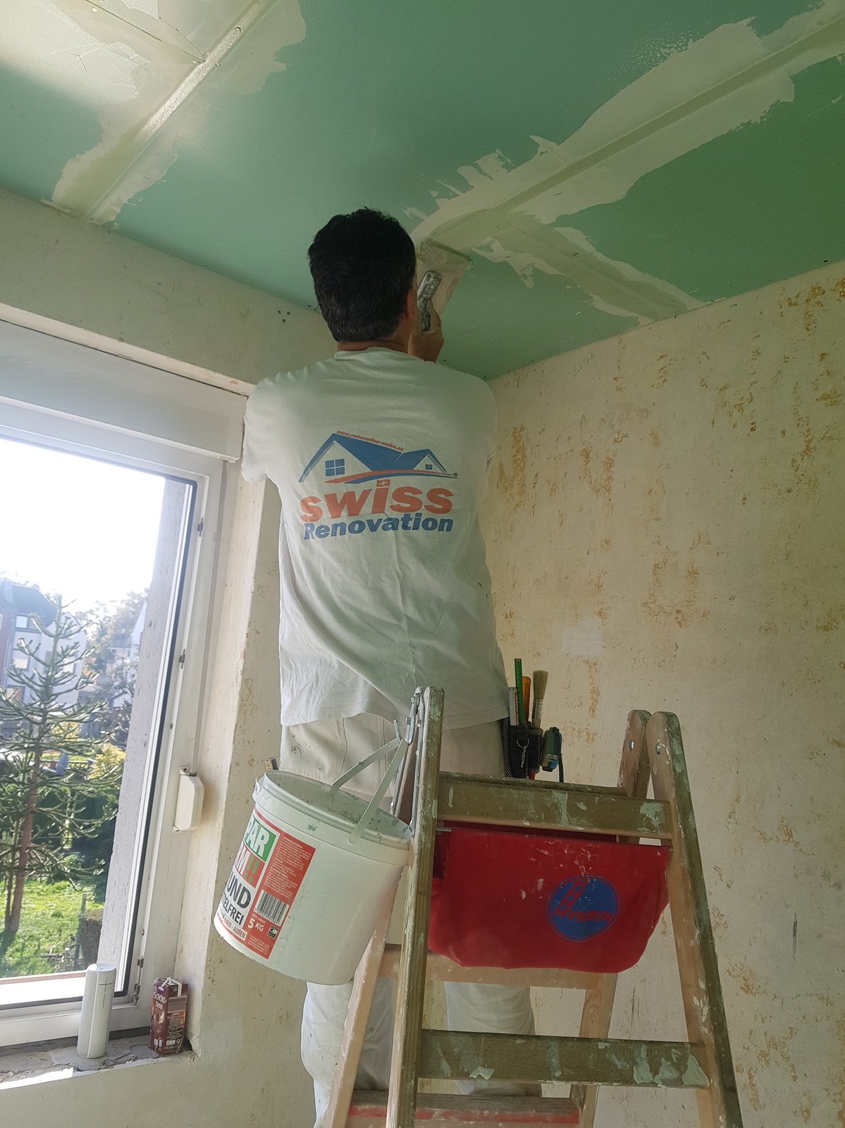 Mitarbeiter beim Streichen einer Decke auf der Leiter